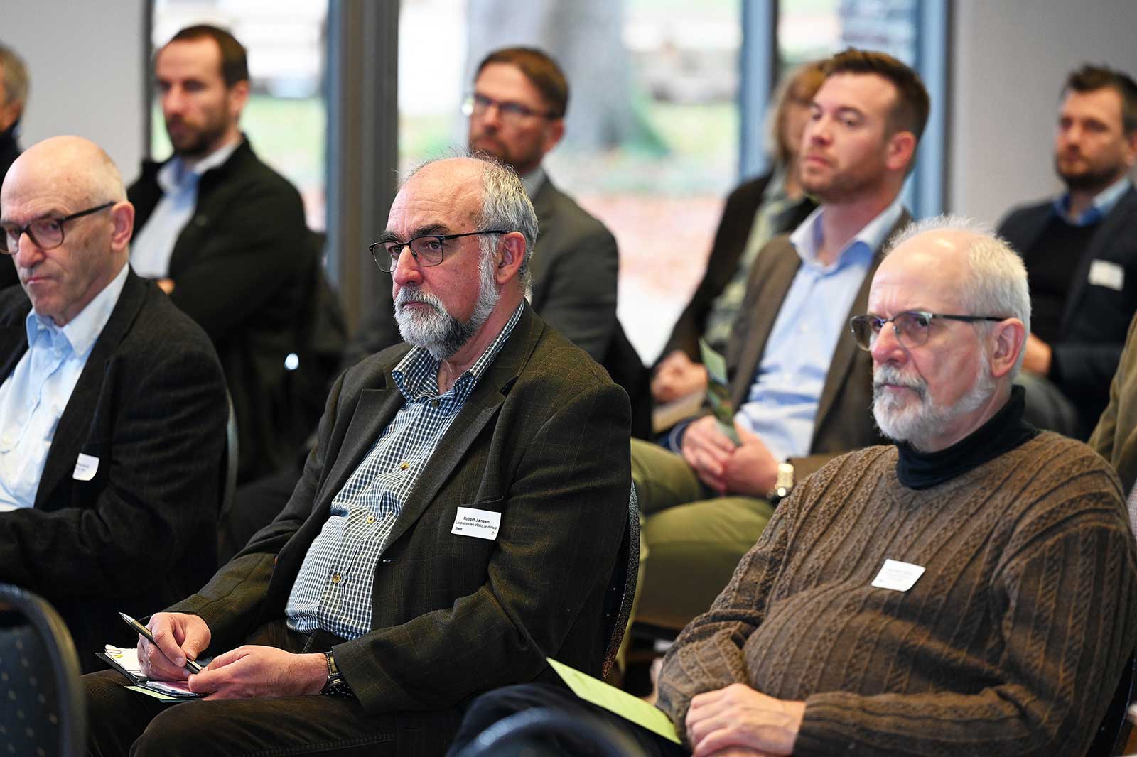 Eine Gruppe von Menschen sitzt in einem Innenraum und ist in eine Diskussion vertieft, mit Namensschildern auf ihrer Kleidung.