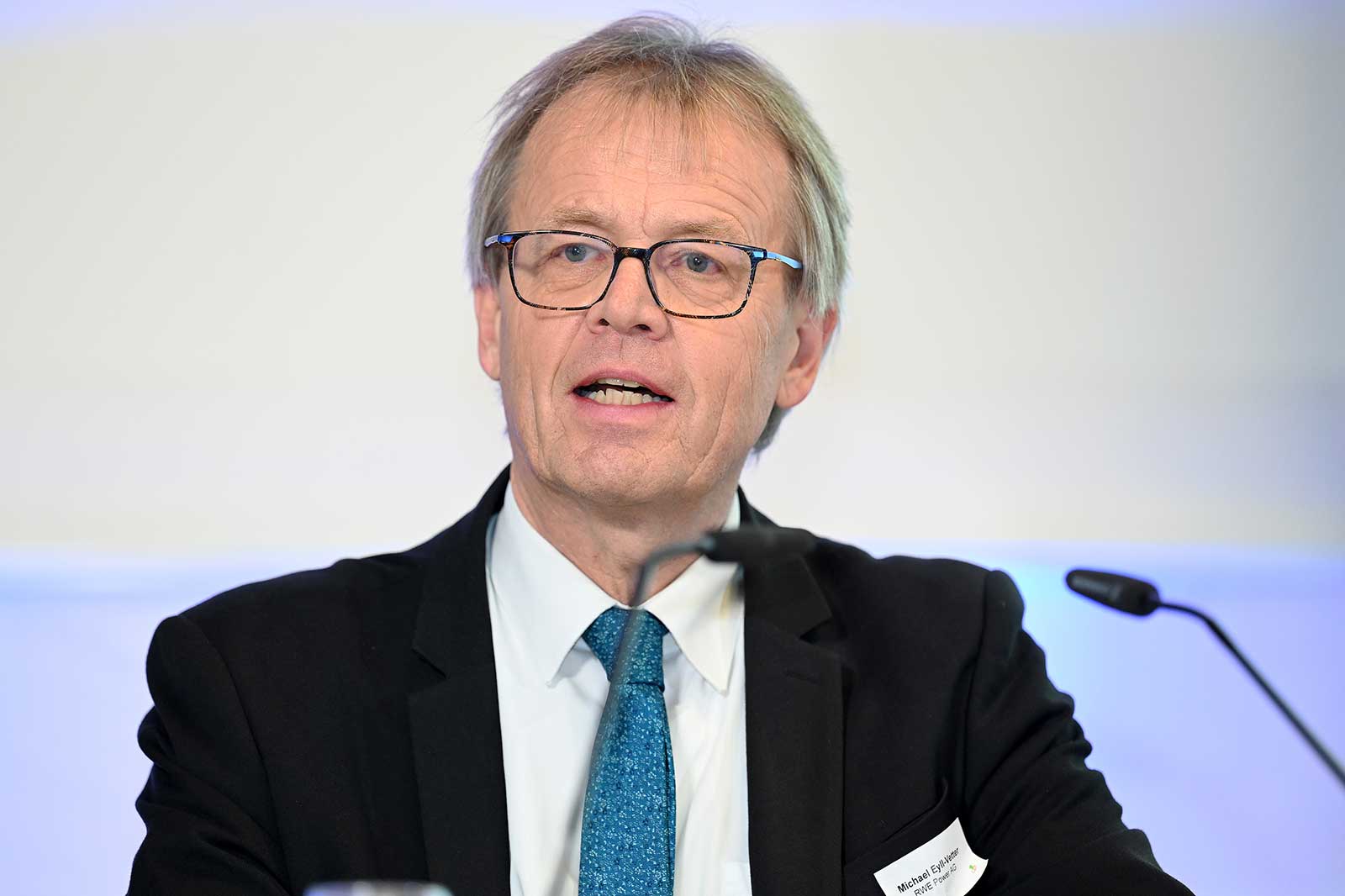 Ein Mann in einem Anzug mit einer blauen Krawatte sitzt an einem Konferenztisch und diskutiert wichtige Themen.