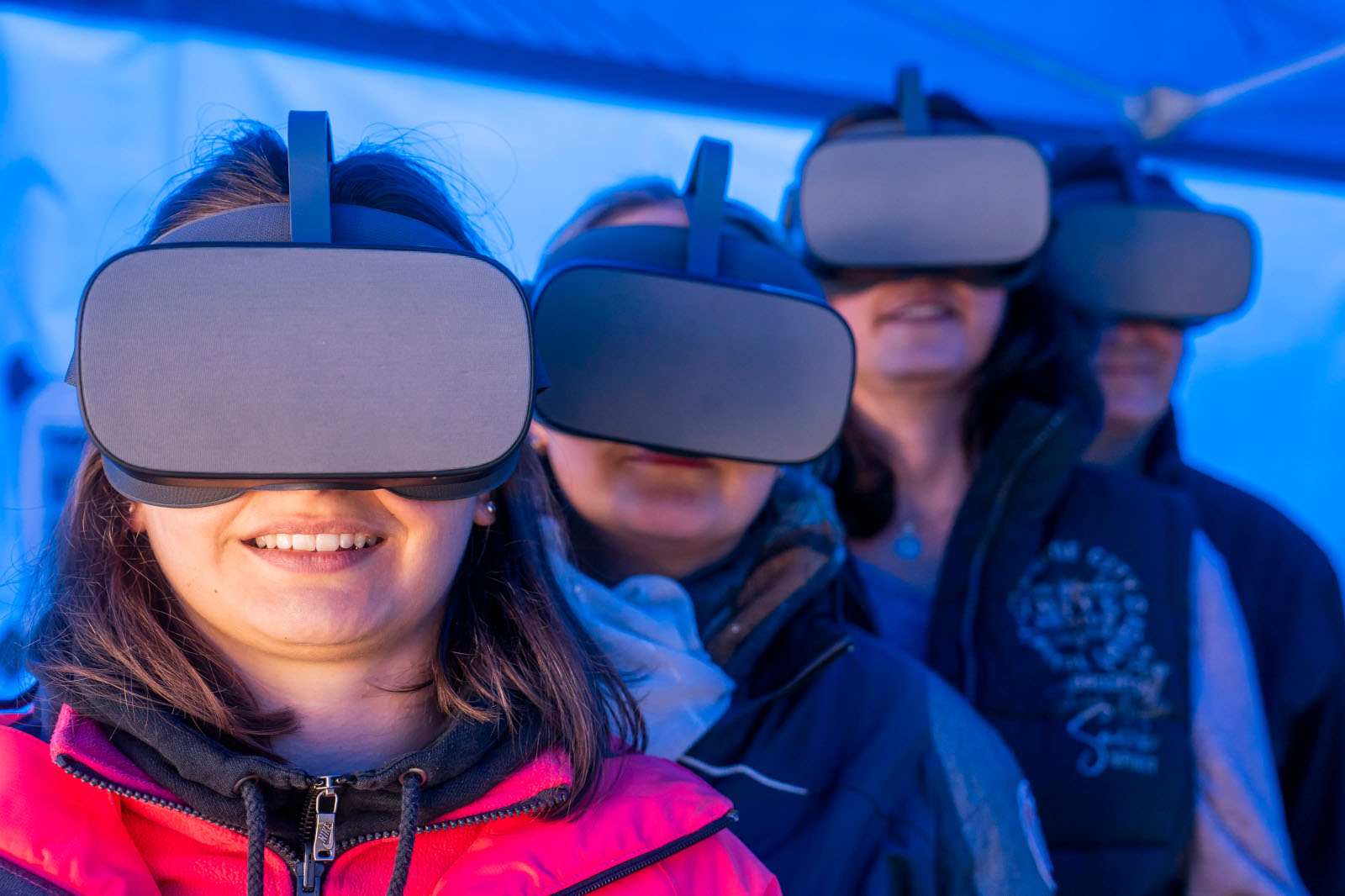 Eine Gruppe von Menschen trägt in einer blau beleuchteten Umgebung Virtual-Reality-Headsets und ist in ein immersives Erlebnis vertieft.