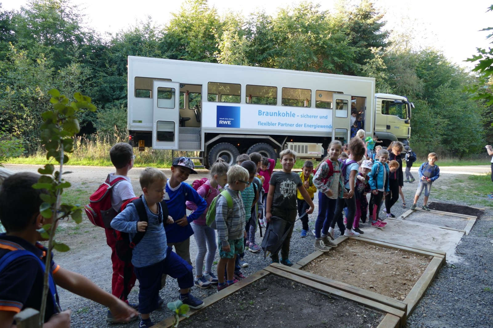 Eine Gruppe von Kindern in einem Waldgebiet stellt sich in einer Reihe neben einem Lastwagen mit einem RWE-Schild auf.