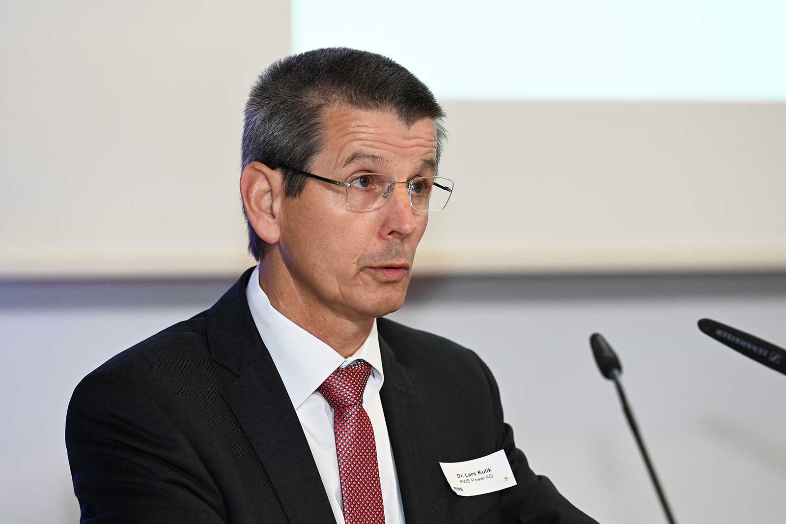 Ein Mann im Anzug und mit roter Krawatte sitzt an einem Mikrofon, mit einem Namensschild 'Dr. Lars Kulik, RWE Power AG'.