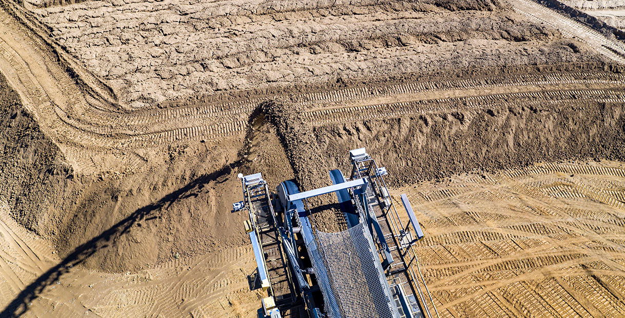Eine Vogelperspektive auf Baumaschinen auf einem sandigen Gelände, mit frisch bewegter Erde und sichtbaren Reifenspuren.