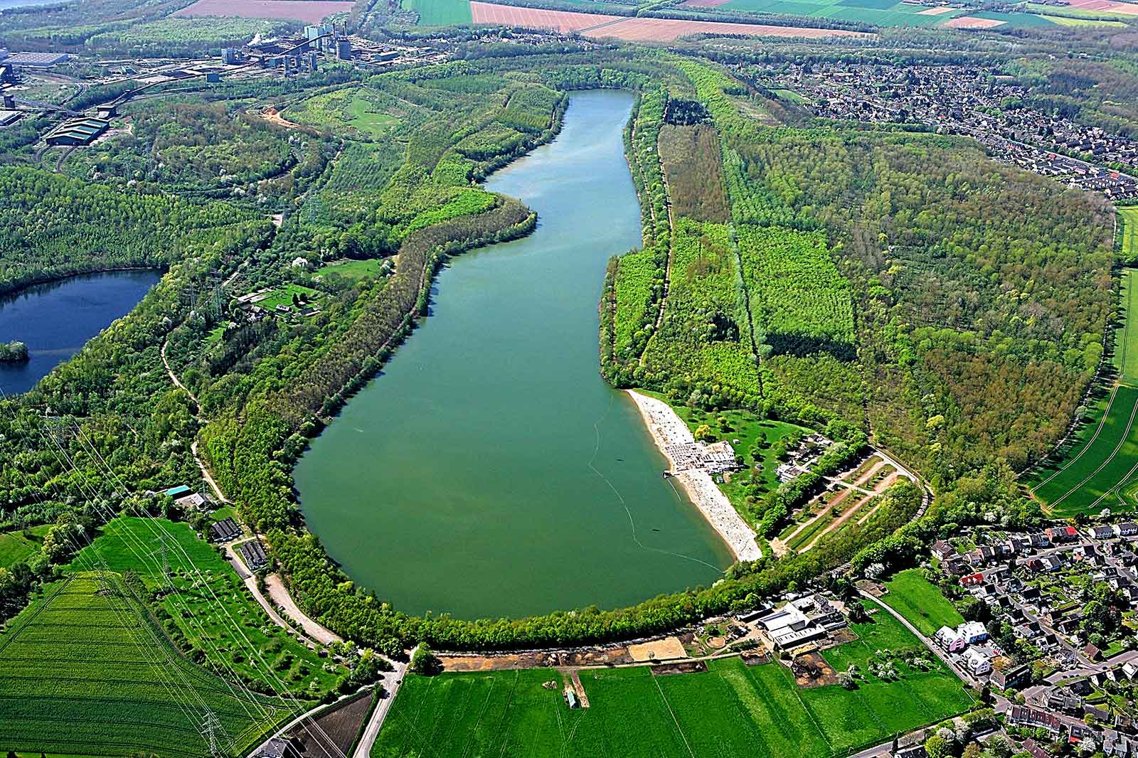 Eine Luftaufnahme eines gewundenen Flusses, umgeben von üppigem Grün und Landwirtschaft. Ein Sandstrandbereich ist in der Nähe des Wassers sichtbar.