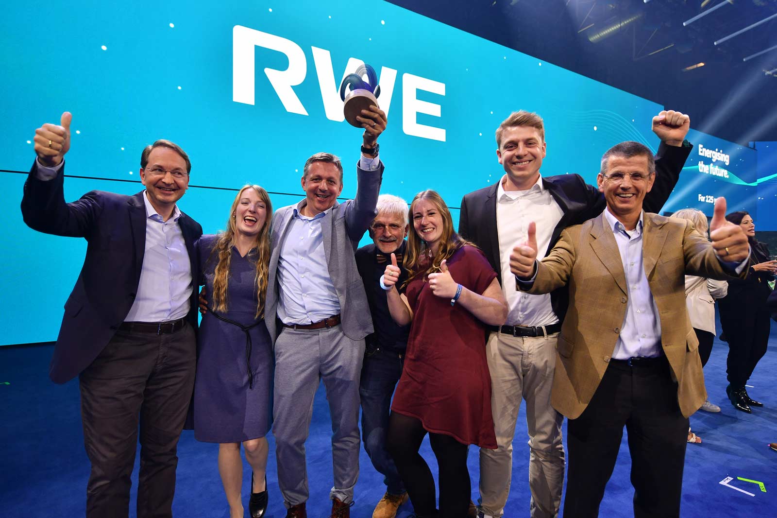 Eine Gruppe von Menschen feiert mit einer Trophäe bei einer Veranstaltung mit RWE-Branding im Hintergrund.