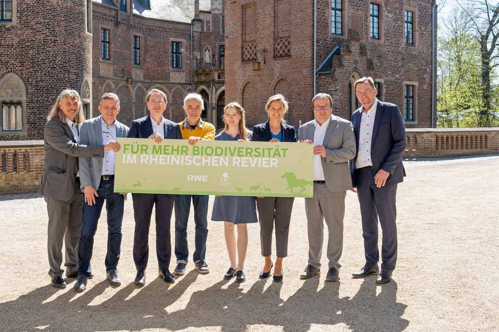 Gruppe von Menschen, die ein Schild mit der Aufschrift 'Für mehr Biodiversität im rheinischen Revier' halten.
