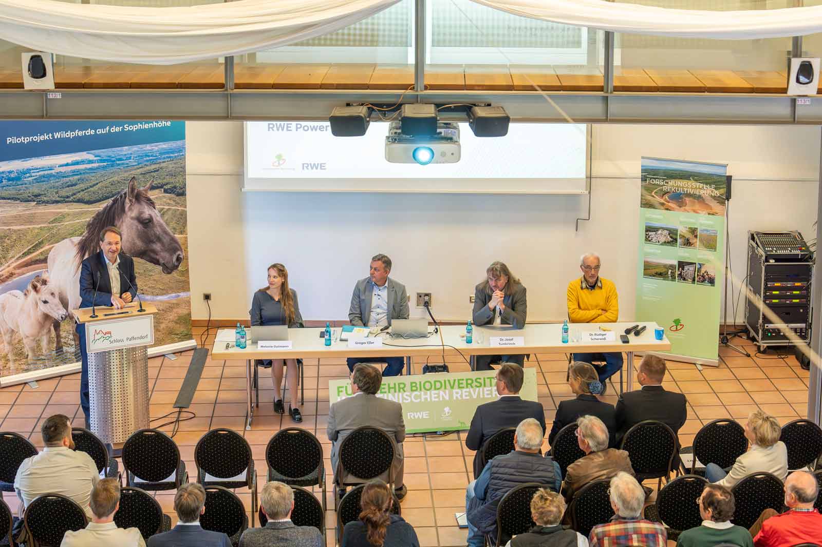 Eine Podiumsdiskussion auf einer Konferenz mit Rednern und einem Publikum in einem gut beleuchteten Raum mit pferdebezogenen Dekorationen.
