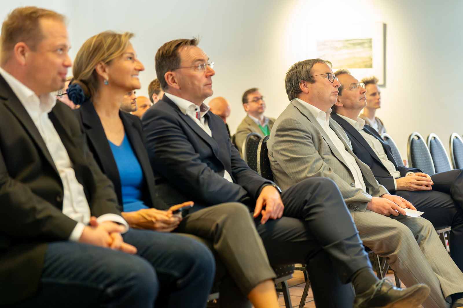 Eine Gruppe von Menschen sitzt in einem Konferenzraum, gekleidet in formelle Kleidung, und ist in eine Diskussion vertieft.