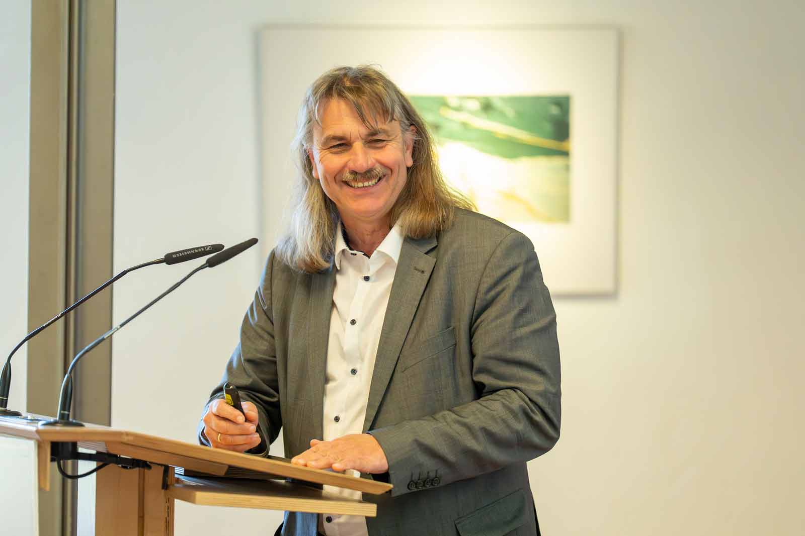 Ein Mann mit langen Haaren steht an einem Podium, hält einen Stift und bereitet sich darauf vor, auf einem Notizblock zu schreiben.