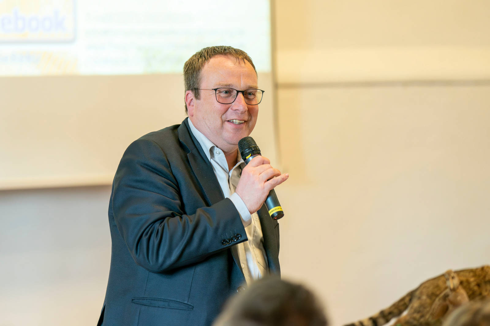 Ein Sprecher mit Mikrofon präsentiert in einem Konferenzraum, der mit einem Tigerskin dekoriert ist.